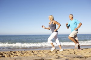 Senior Couple In Fitness Clothing Running Along Beach